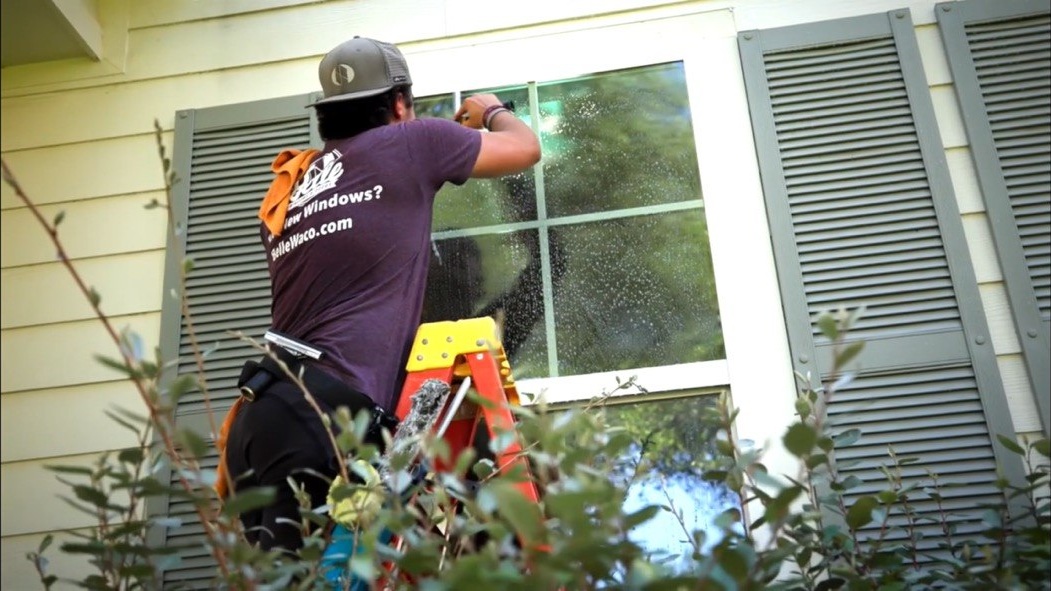 Belle technician cleaning a residential window from a ladder